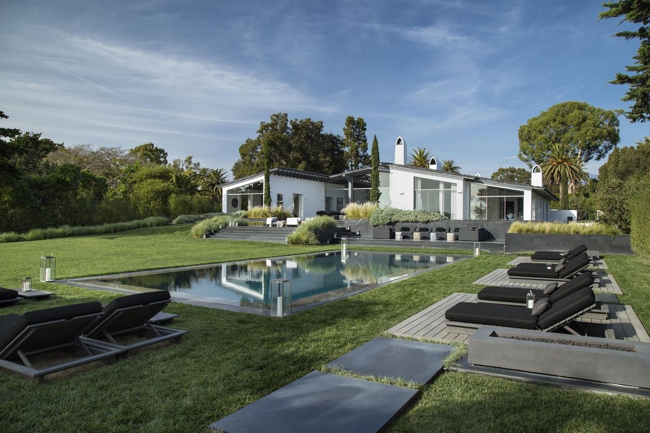 A luxurious Hope Ranch Santa Barbara estate home in the background, with a bi-level stone terrace, sparkling pool and expansive lawn in the foreground